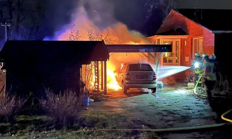 Ein brennendes Auto steht in einem Carport.