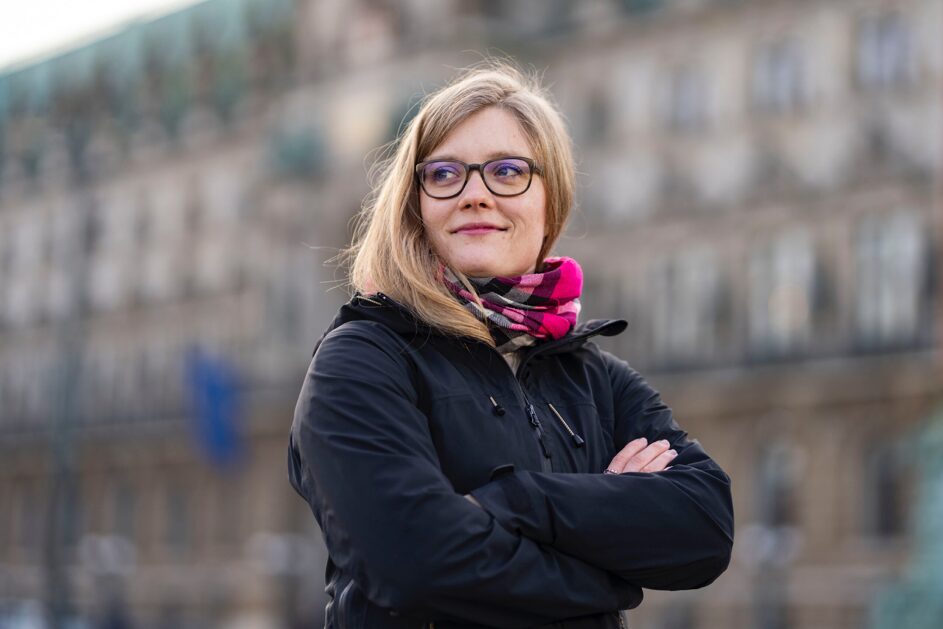 a woman with glasses and a scarf crossing her arms