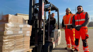 a group of men in orange vests and orange vests standing next to a forklift