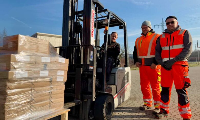 a group of men in orange vests and orange vests standing next to a forklift