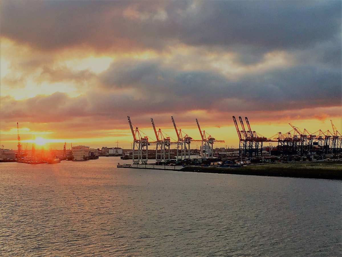 a sunset over a body of water with cranes