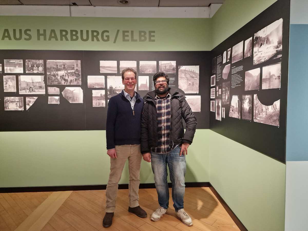 two men standing in a room with pictures on the wall