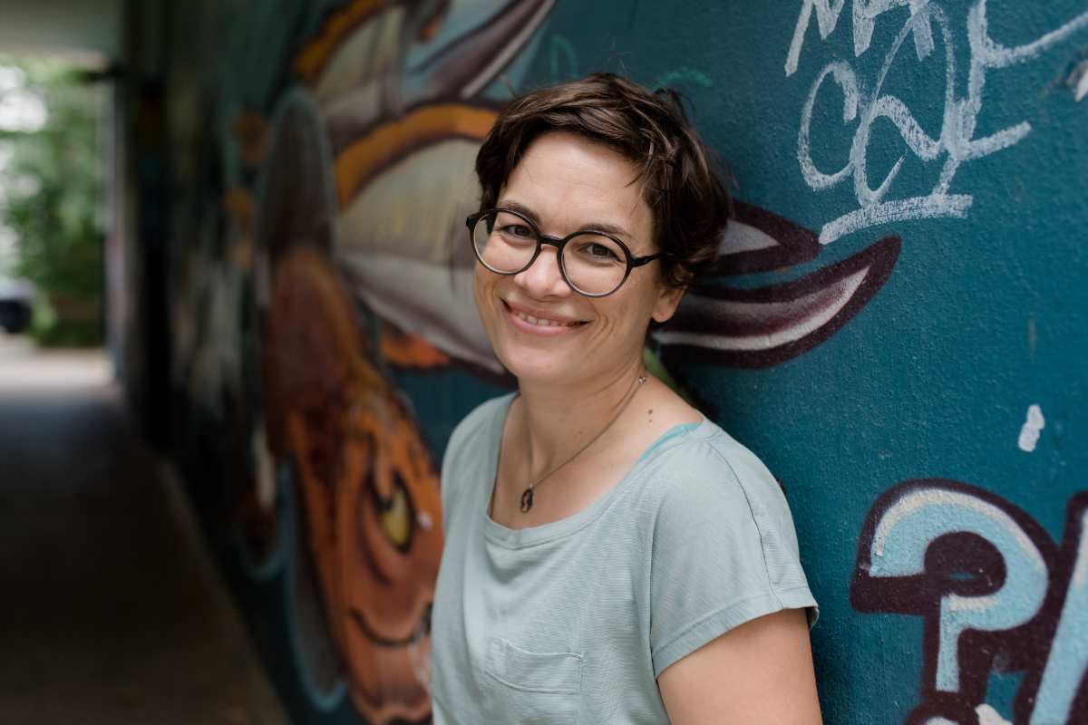 a woman smiling in front of a wall with graffiti