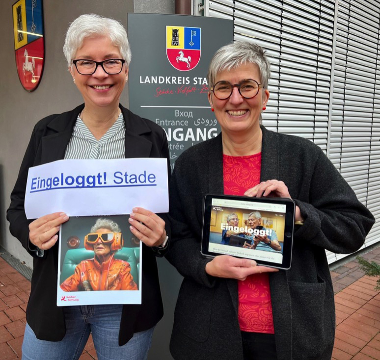 two women holding a tablet and a sign