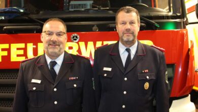 two men in uniform standing in front of a firetruck