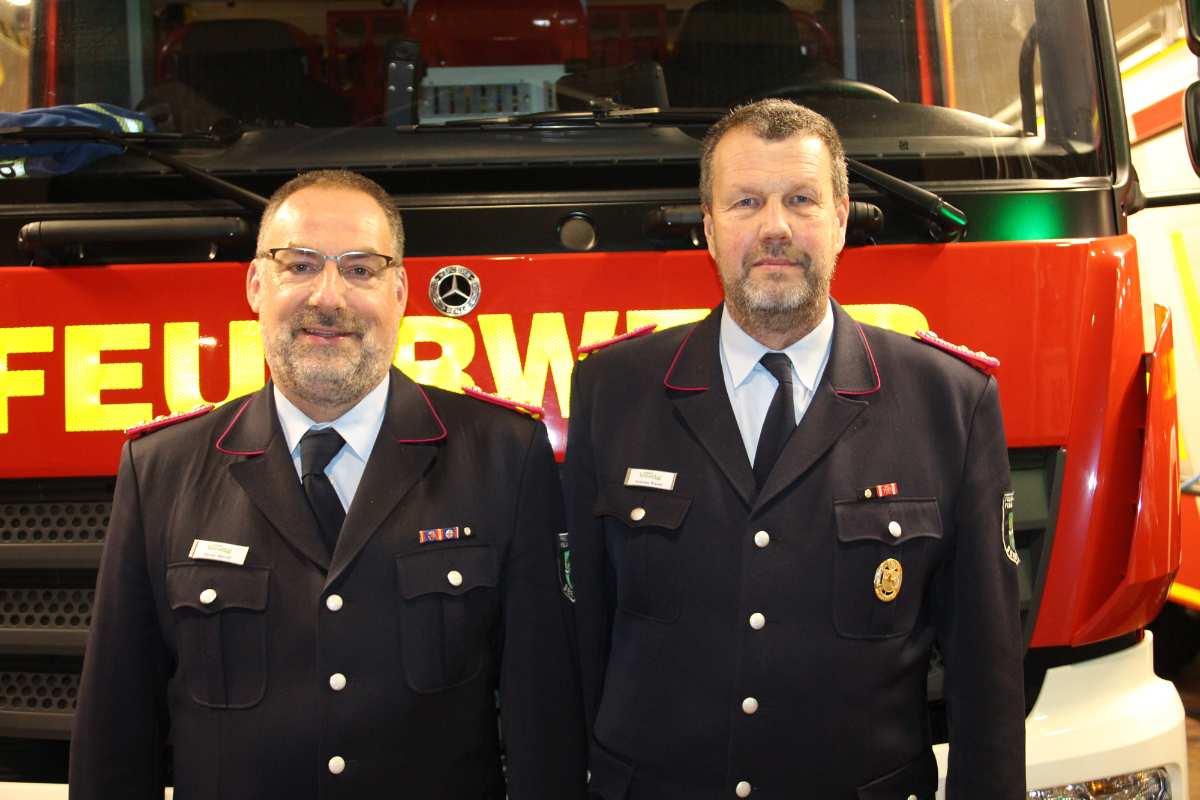 two men in uniform standing in front of a firetruck