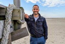 a man leaning against a wooden post on a beach