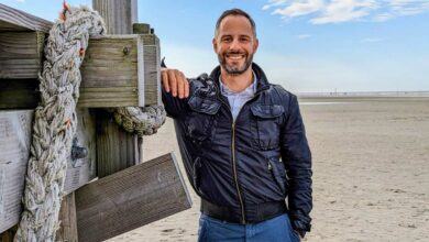 a man leaning against a wooden post on a beach