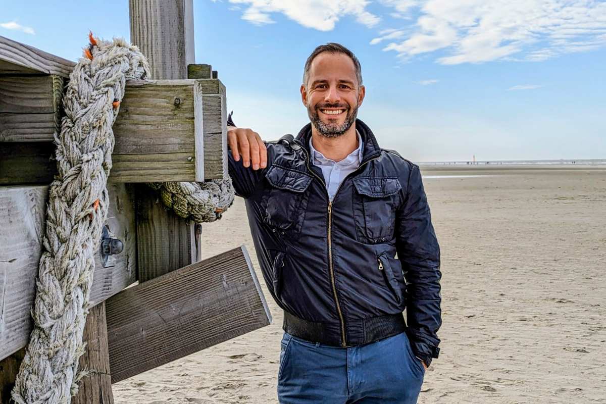 a man leaning against a wooden post on a beach