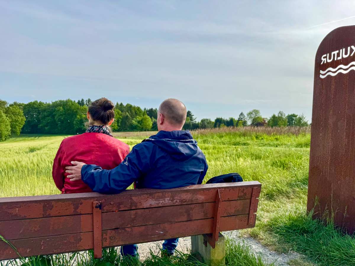 a man and woman sitting on a bench in a field
