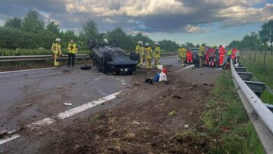 a car crashed into a road with firemen and a group of people