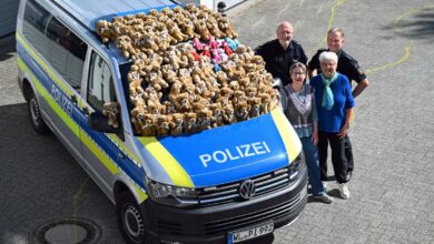 a group of people standing next to a police van with teddy bears on the roof