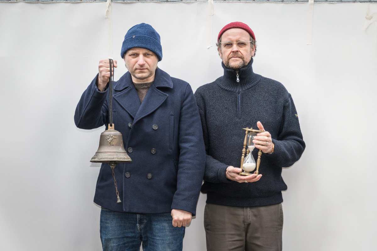 two men holding an hourglass and a bell