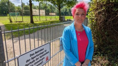 a woman with pink hair standing in front of a fence
