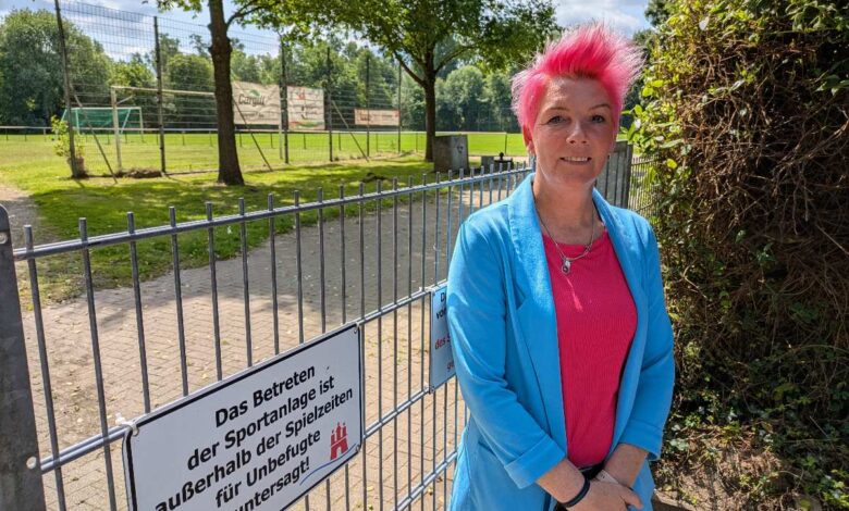 a woman with pink hair standing in front of a fence