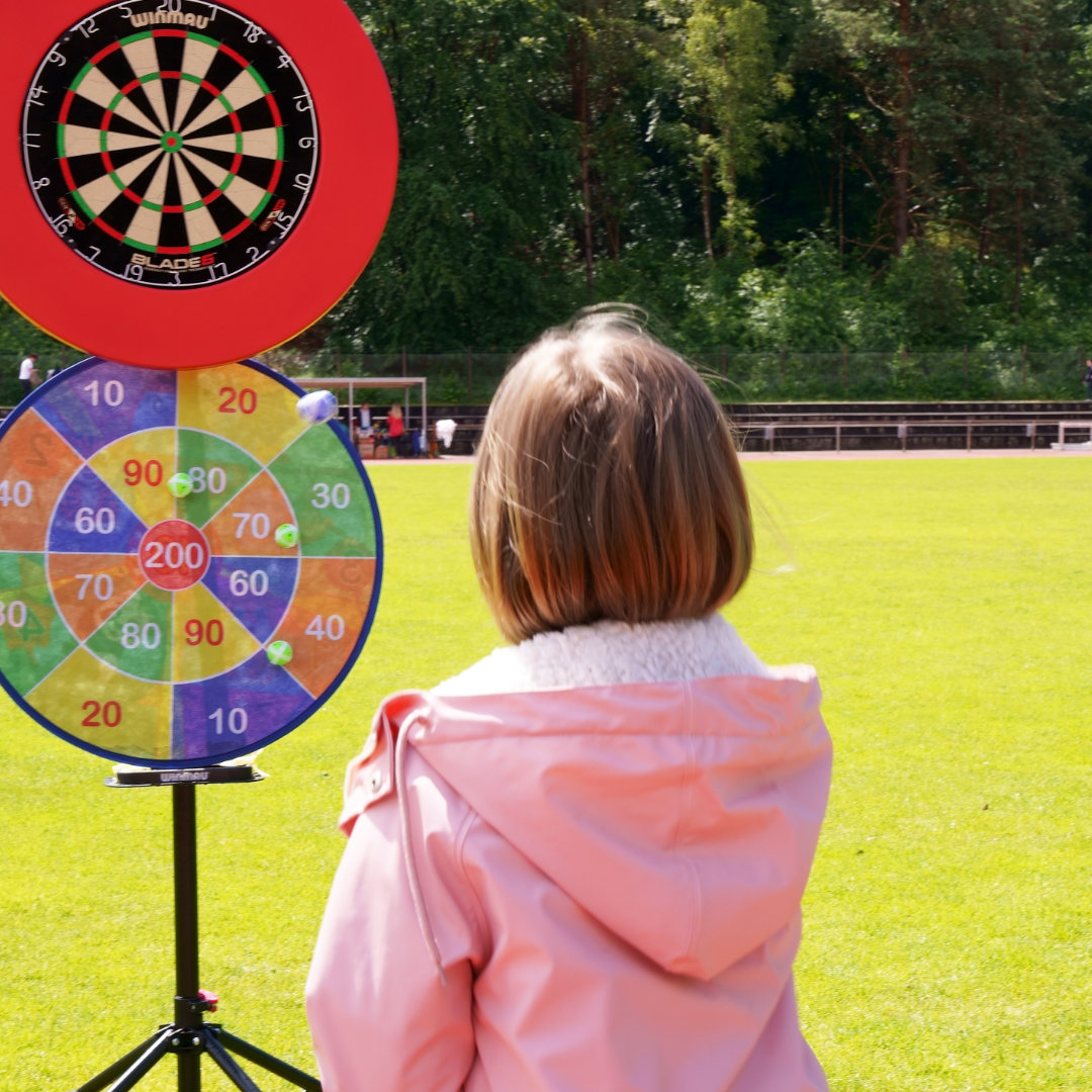 a girl in a pink jacket sitting in front of a dart board
