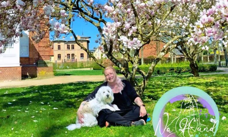 a woman sitting on a bench with a dog under a tree