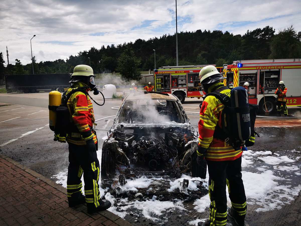firefighters standing next to a burned car