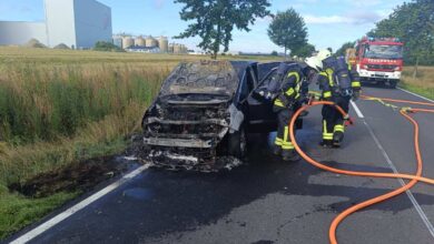 firefighters putting out a burnt out car on a road