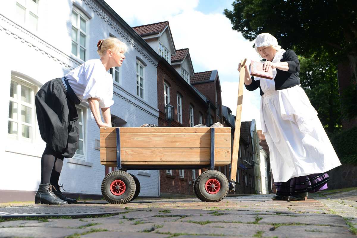 a woman pushing a wooden cart with a woman in a white dress