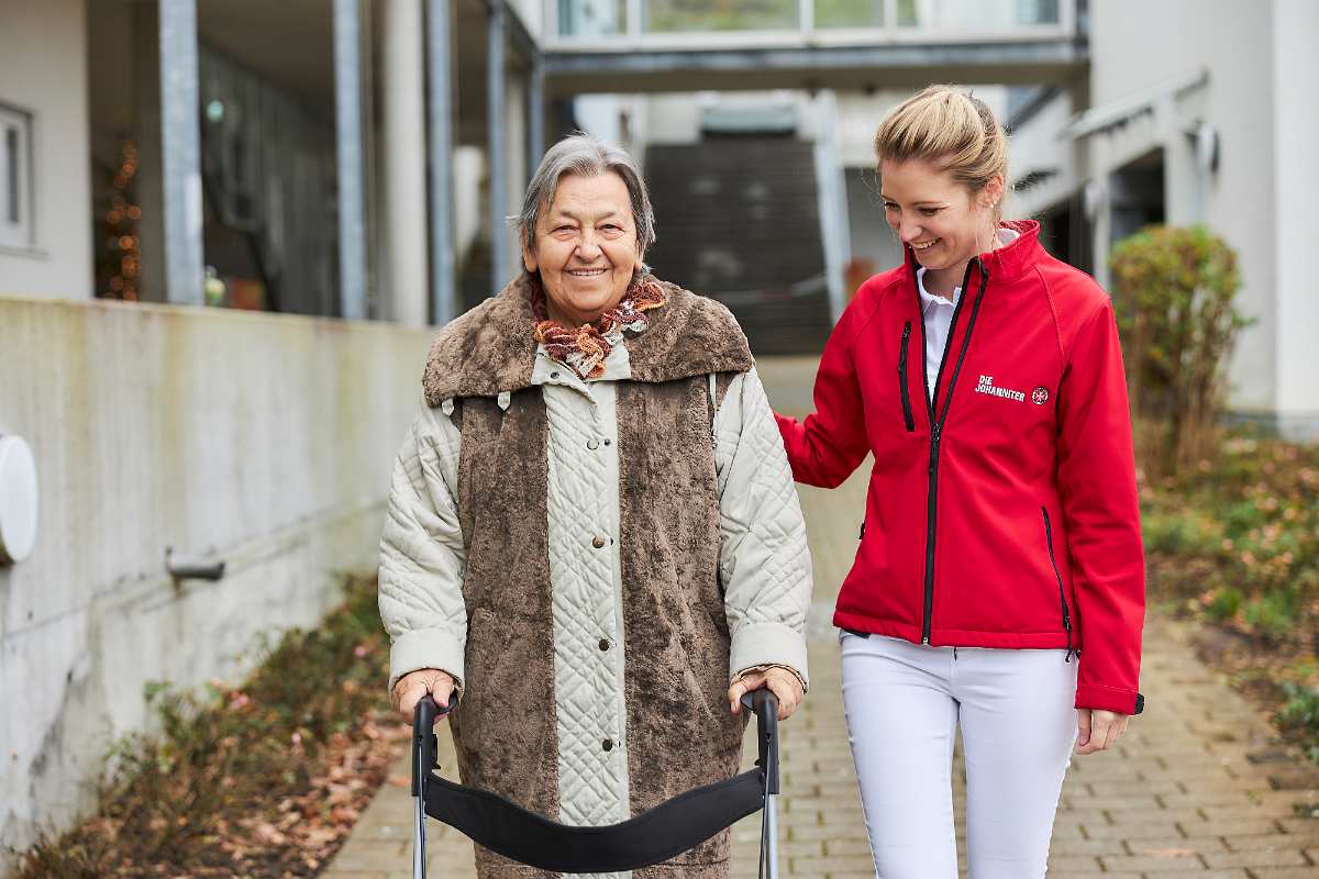 Pflegekraft unterstützt ältere Dame beim Gehen.
