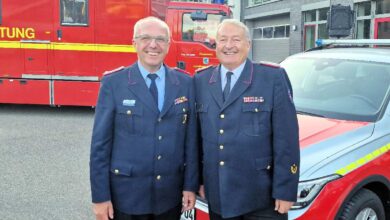 Zwei Feuerwehrmänner vor Einsatzfahrzeugen.
