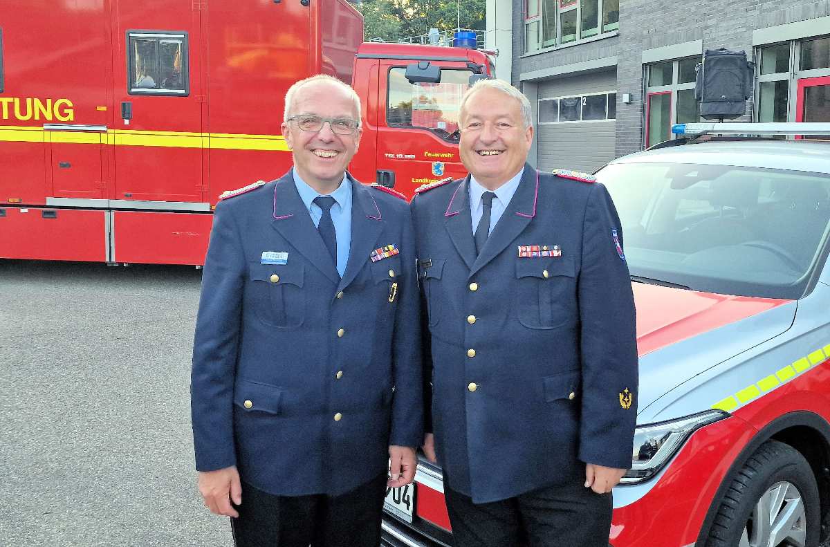 Zwei Feuerwehrmänner vor Einsatzfahrzeugen.