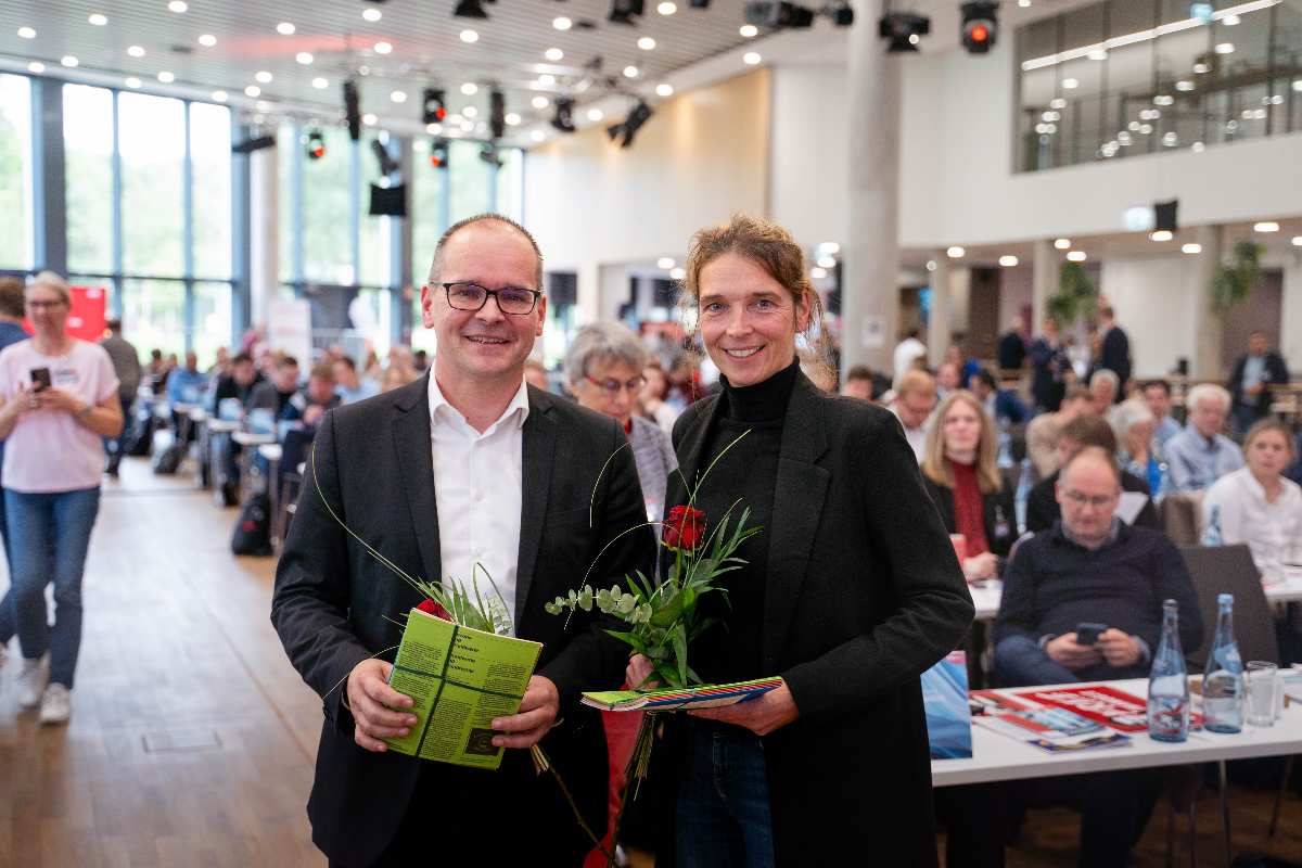 Zwei Personen mit Blumen und Unterlagen.