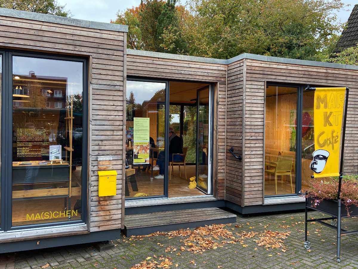 Kaffeetafel und Klanggenuss: Pop-up-Box Maschen feiert Neustart am 25. Oktober 1 Holzgebäude mit Café und Pflanzen