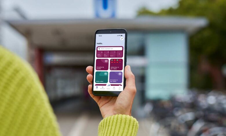 hvv switch-App wird zum digitalen Herzstück der Hamburger Mobilität mit neuem Ticketing und Echtzeitdaten 4 Handy mit HVV-App vor Bahnhof
