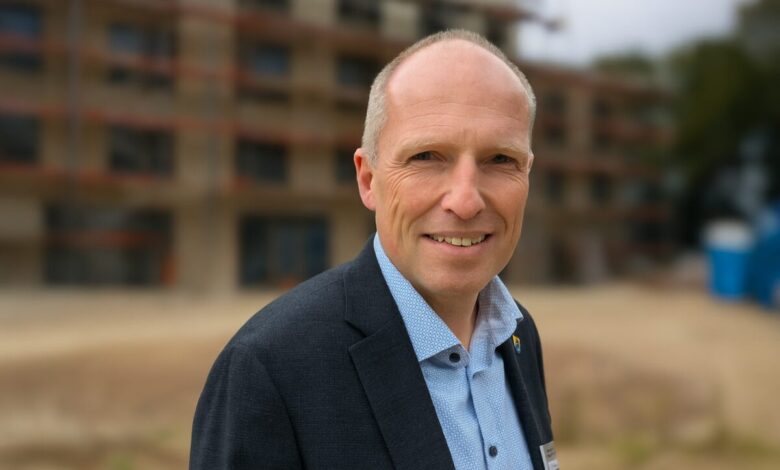 Mann vor Baustelle, seriös gekleidet.