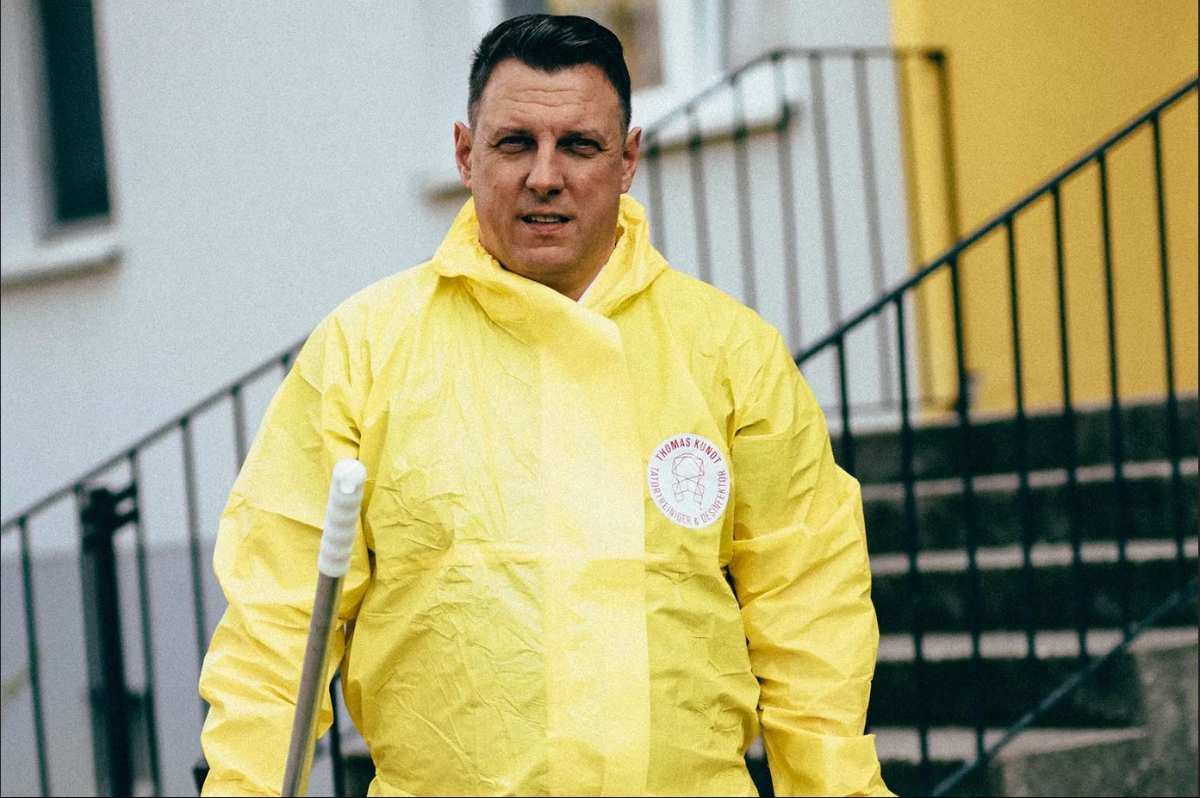 Mann in gelber Schutzkleidung mit Besen.