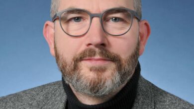 Mann im grauen Anzug, neutraler Hintergrund.