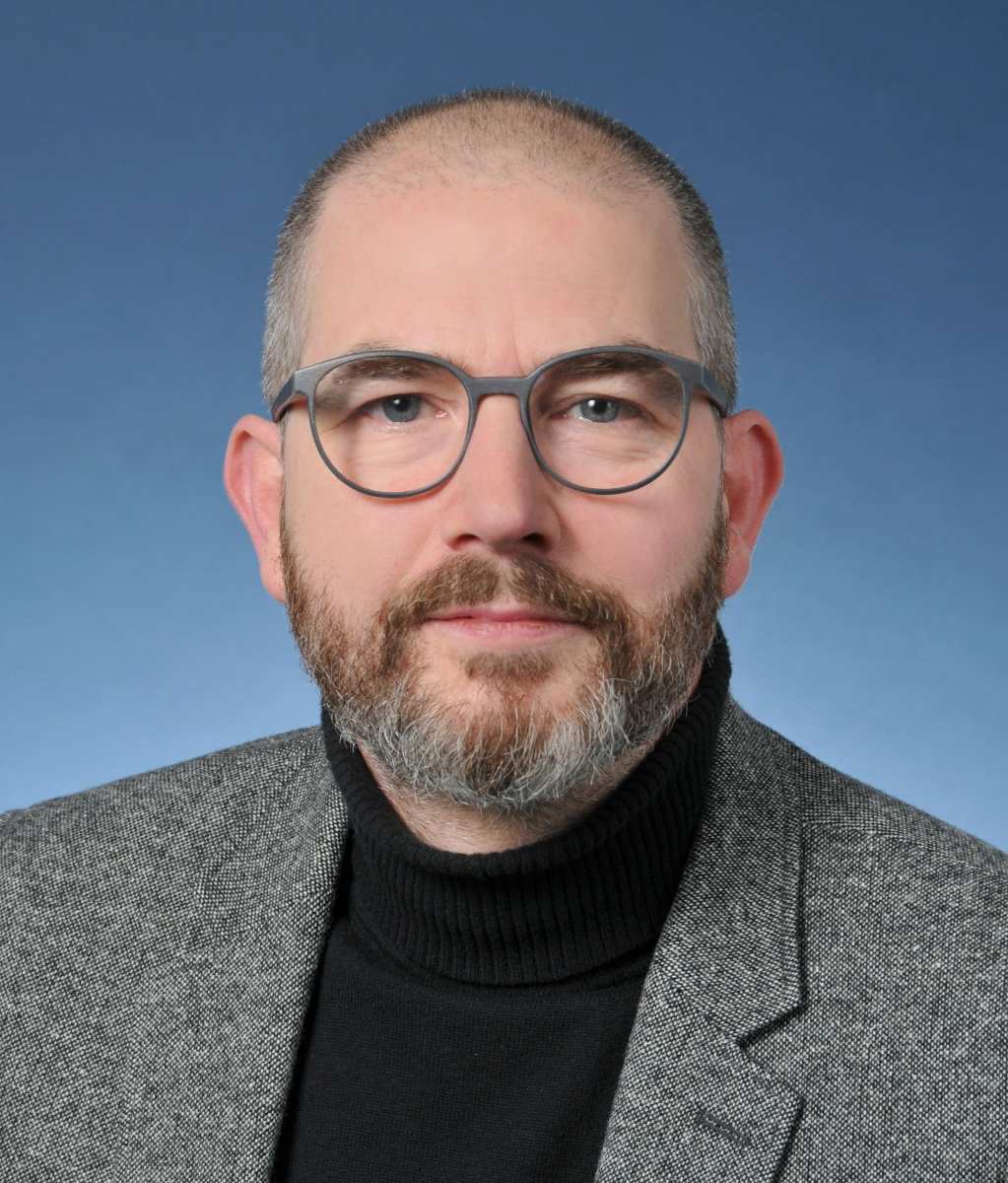 Mann im grauen Anzug, neutraler Hintergrund.